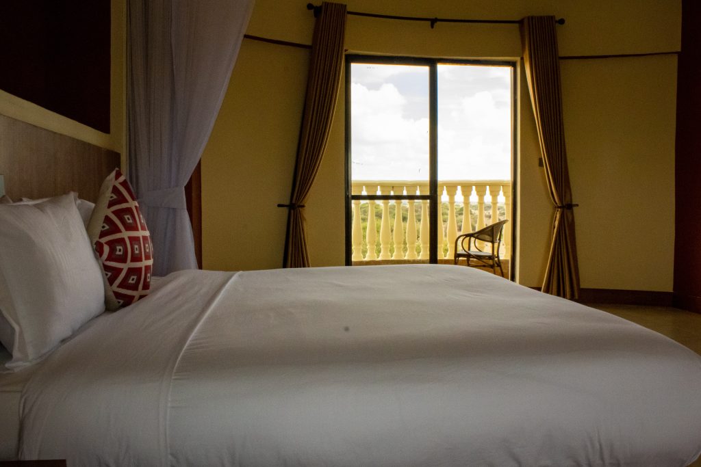 Hotel bedroom with a large bed and balcony overlooking the Amboseli landscape.