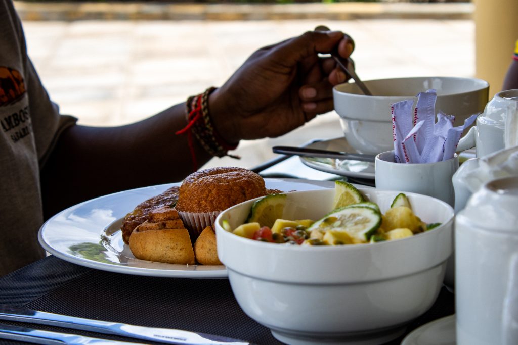 A breakfast spread with fresh fruit salad, muffins, pastries, and a person holding a spoon at a dining table.