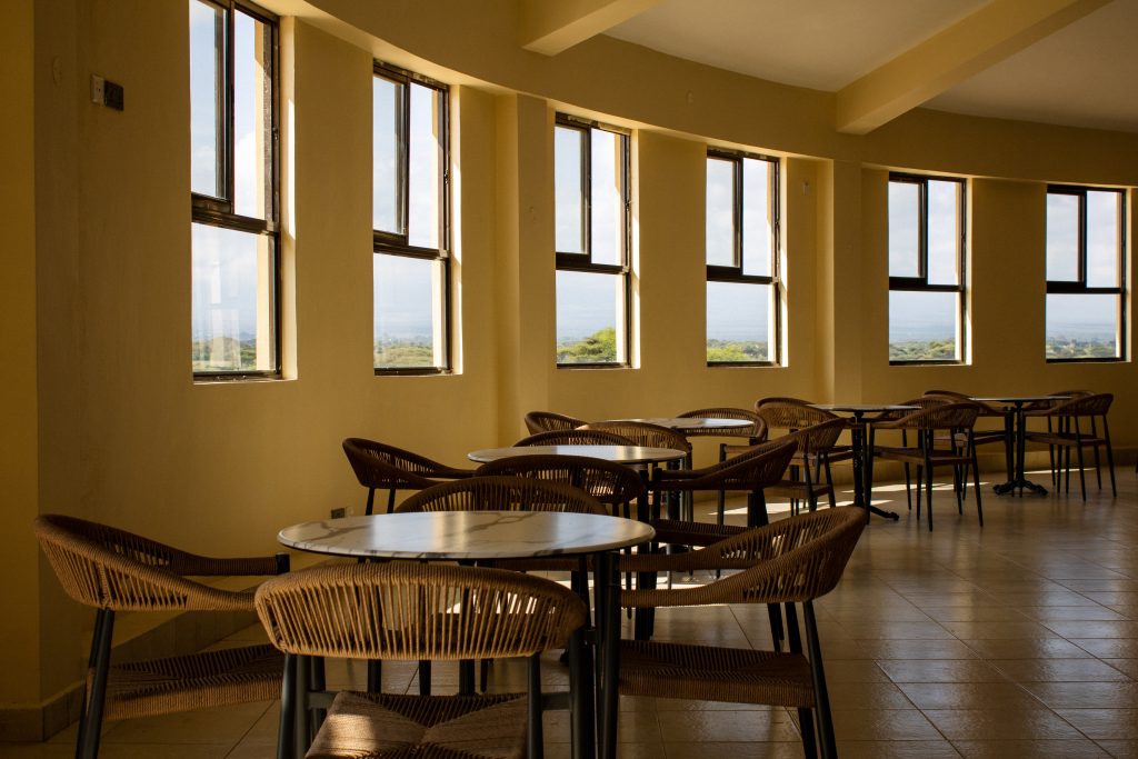 Indoor seating area of Anga Sky Bar featuring woven chairs, dining tables, and tall windows offering scenic views of the surrounding landscape.