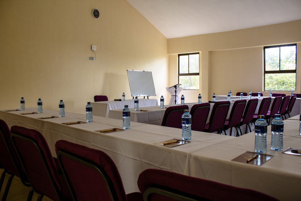 Spacious conference room arranged in a U-shape layout with bottled water, writing pads, a whiteboard, and a podium at the front.