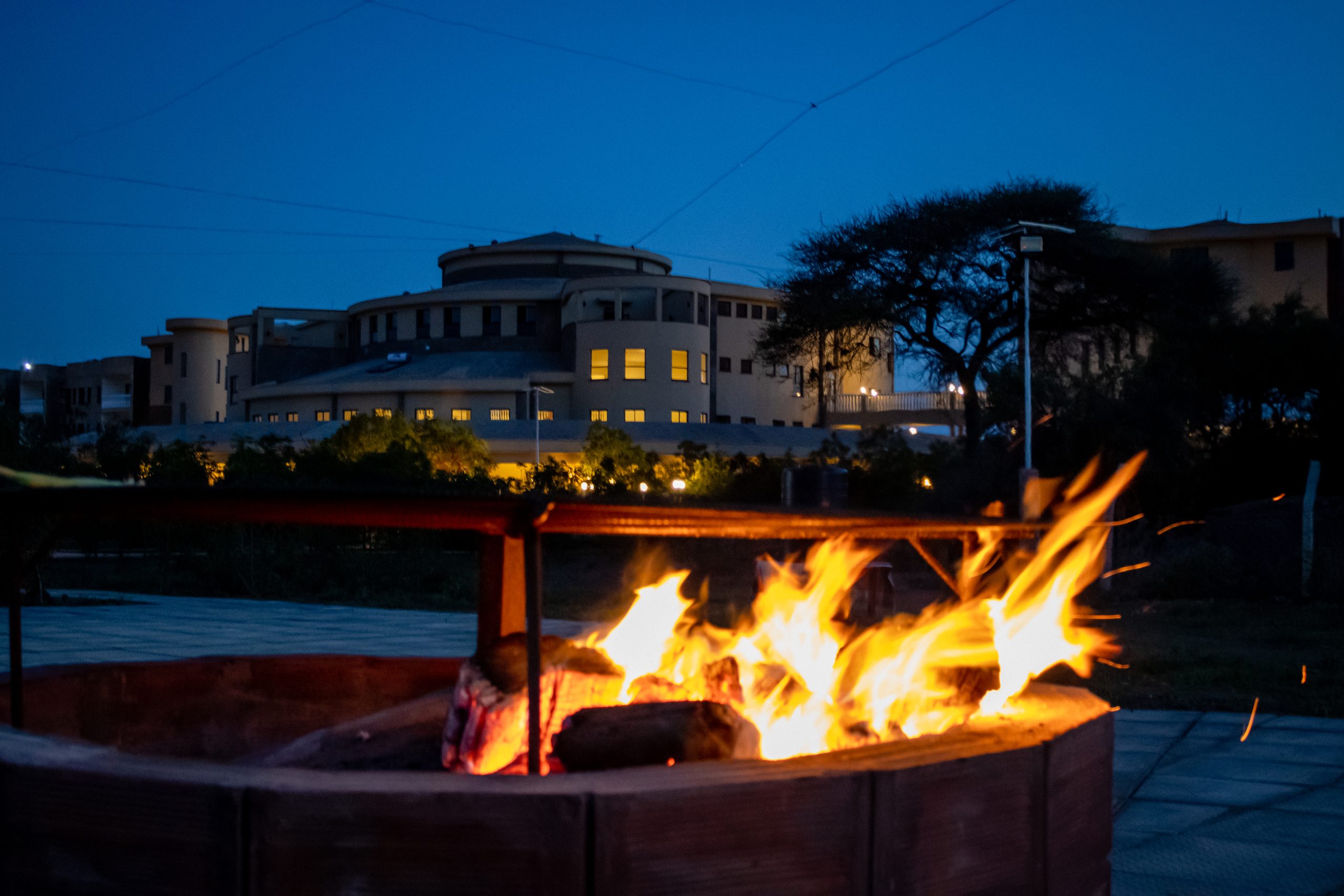 Enkima Firepit glowing with a wood fire at dusk, with the lodge illuminated in the background.