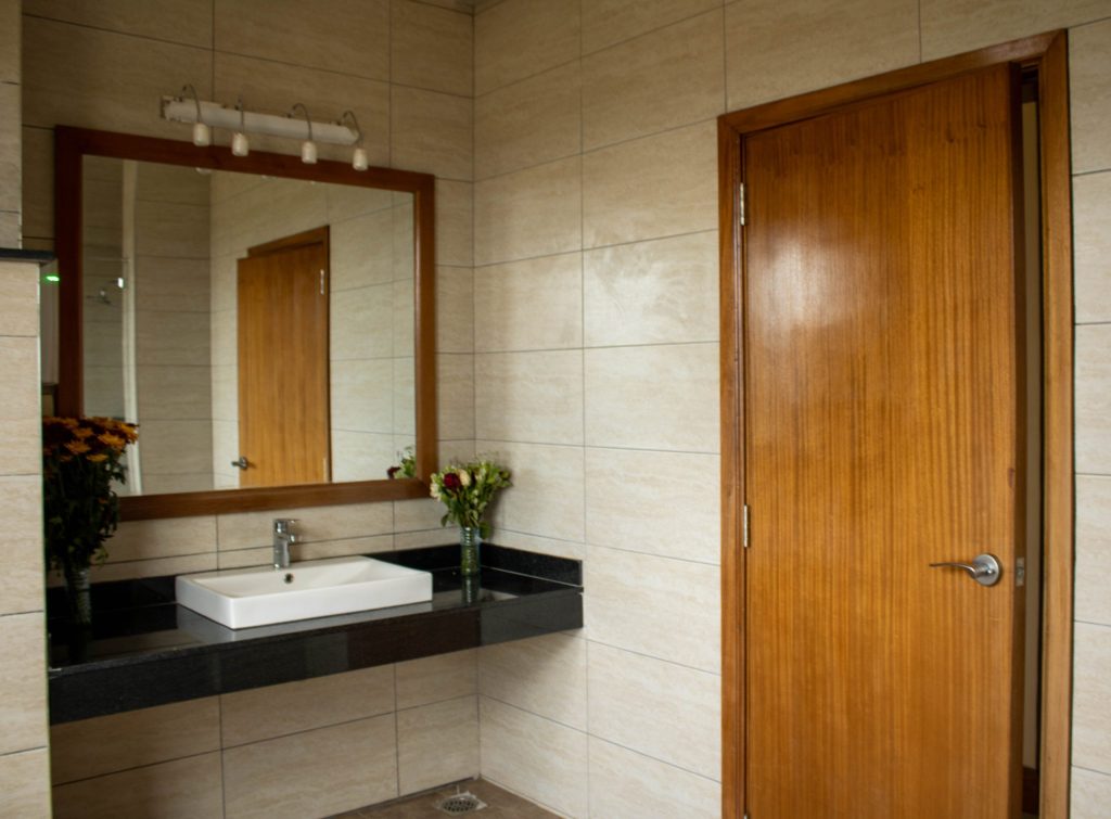 Modern en-suite bathroom featuring a black granite vanity with a vessel sink, large wood-framed mirror, and warm beige wall tiles.