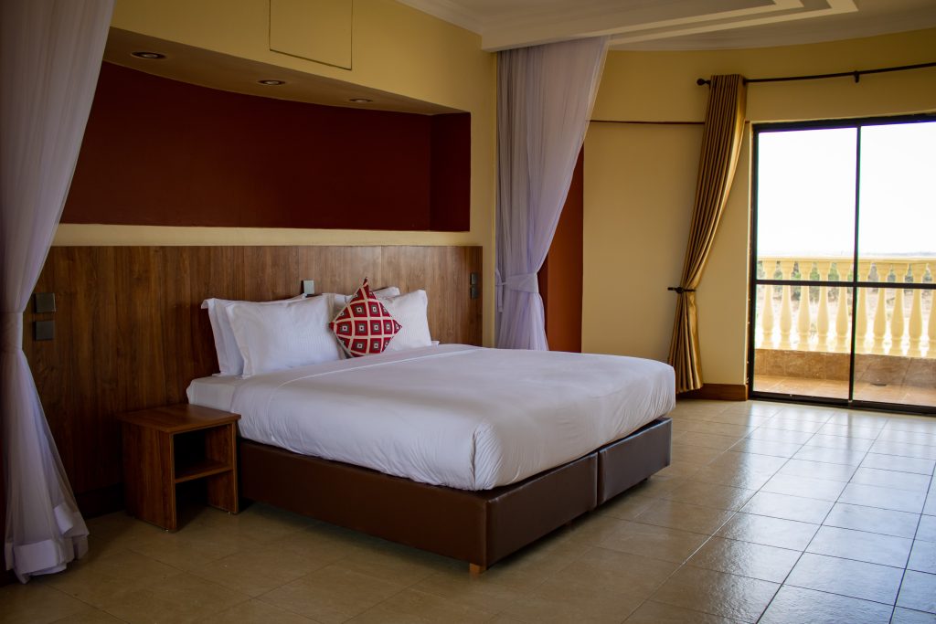 Spacious bedroom with a king bed, wooden headboard, and sliding glass doors leading to a private balcony.