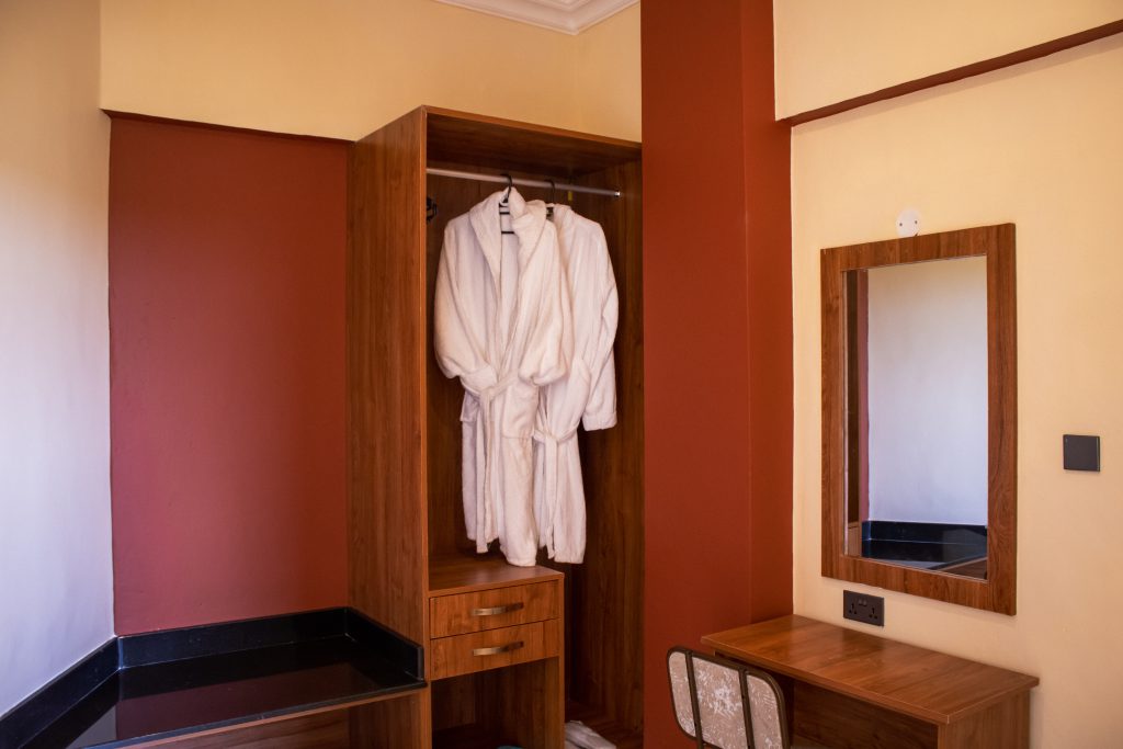 Dressing area in an Executive Terrace Room with a wooden wardrobe, plush white bathrobes, drawers and a vanity table with mirror.