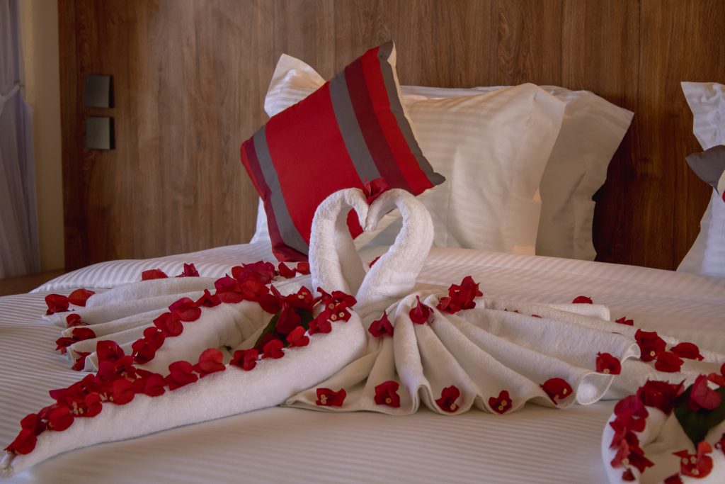 Close-up of a bed decorated with towel swans and fresh flower petals for a romantic turndown service.