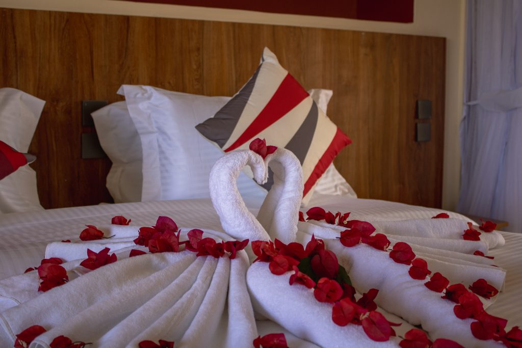 Close-up of a bed decorated with towel swans and fresh flower petals for a romantic turndown service.