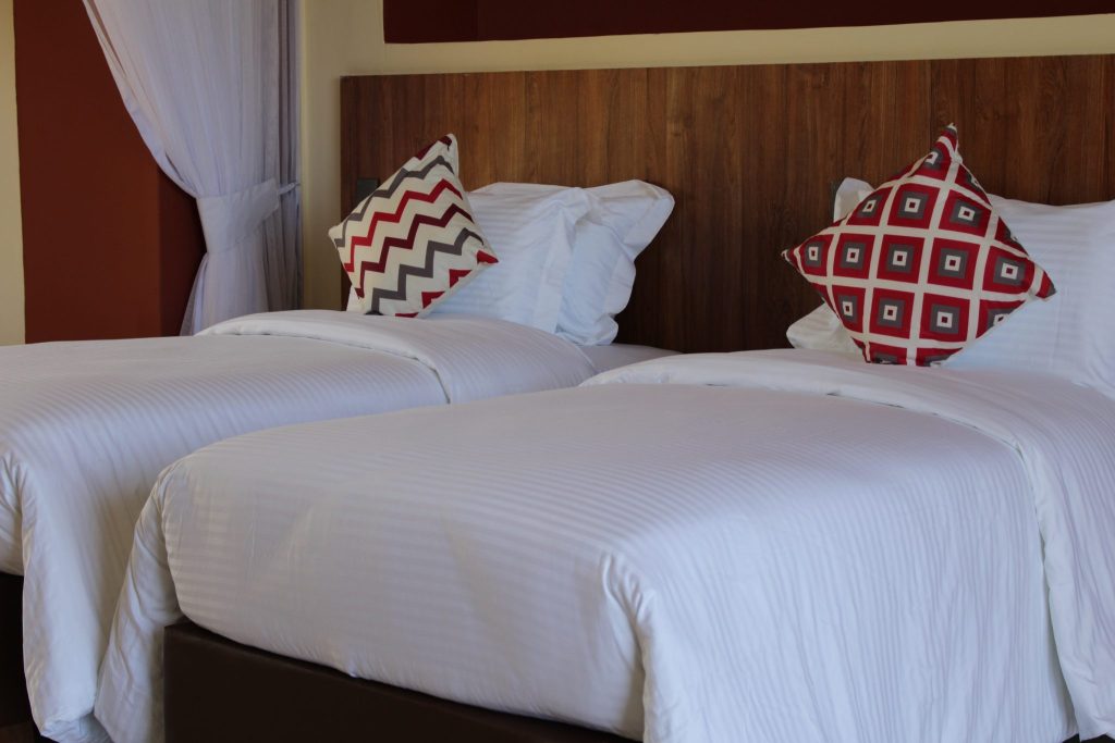 Twin-bed configuration in an Executive Terrace Room, with crisp white linens and decorative red geometric accent pillows against a warm wood headboard.