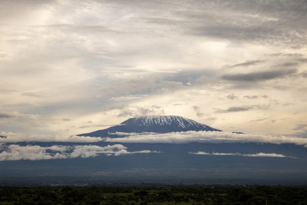 Panoramic view of snow-capped Mount Kilimanjaro framed by cloud layers over the Amboseli landscape.