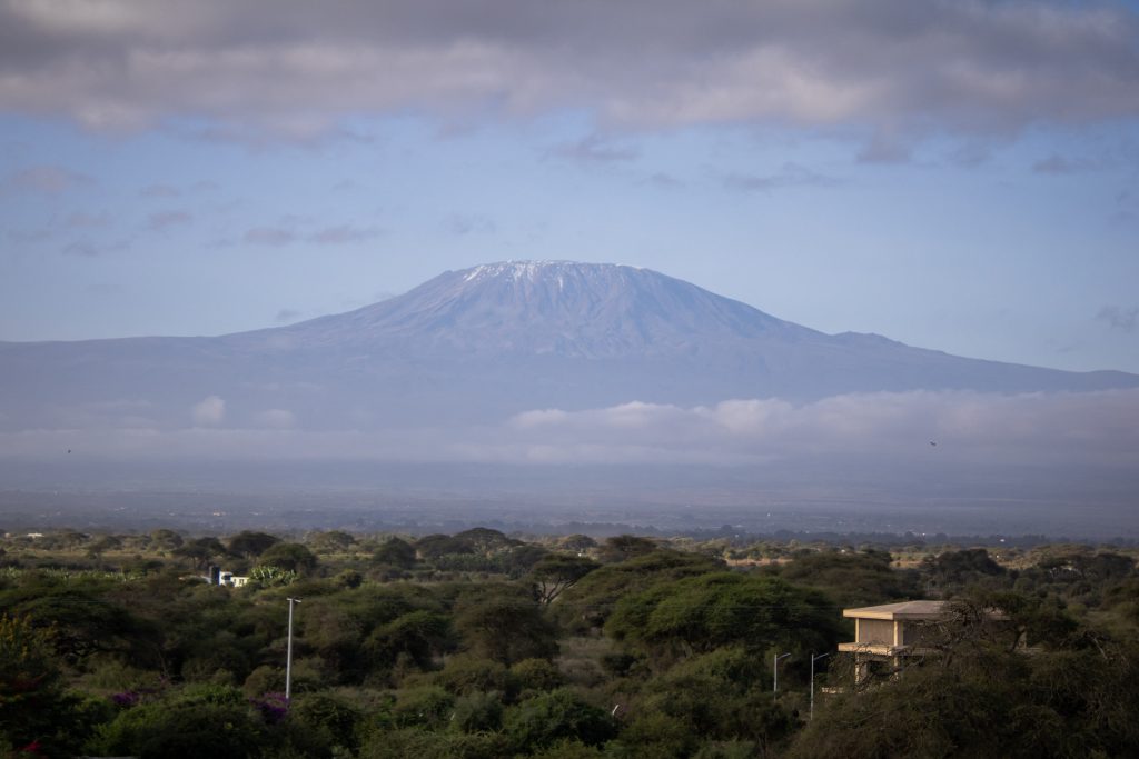 Scenic landscape view of Mount Kilimanjaro rising above cloud layers and green acacia trees in Amboseli.