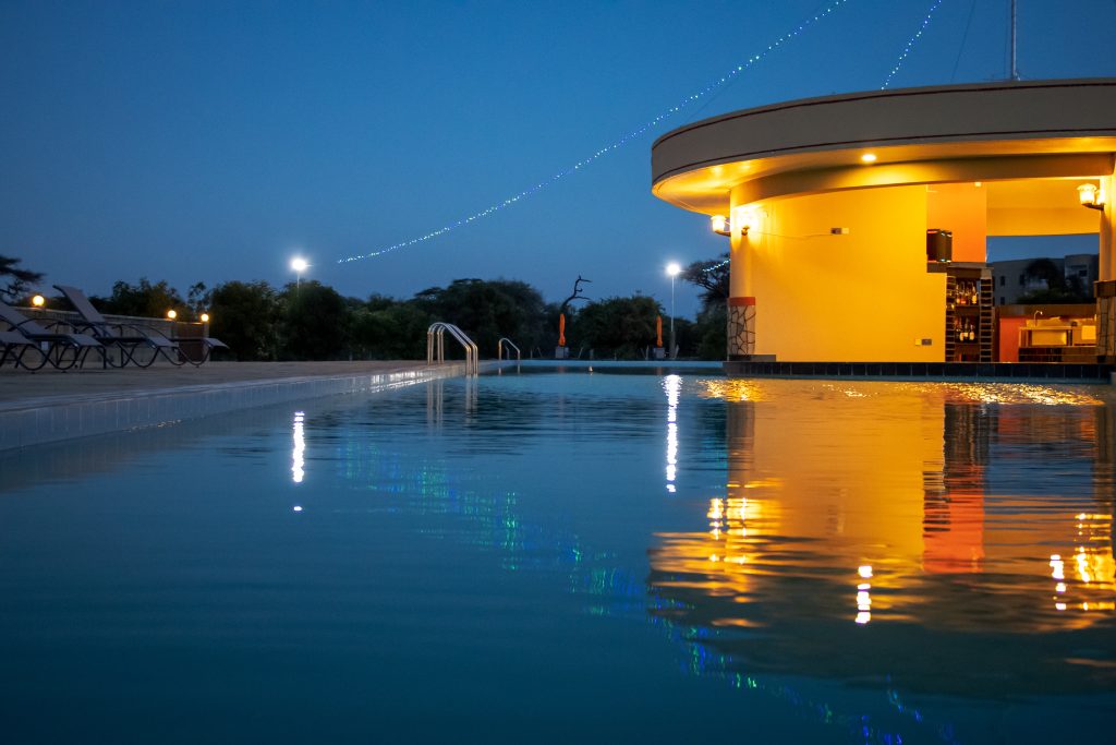 Warmly lit Olkeju swim-up bar reflected in the tranquil waters of the swimming pool at twilight.