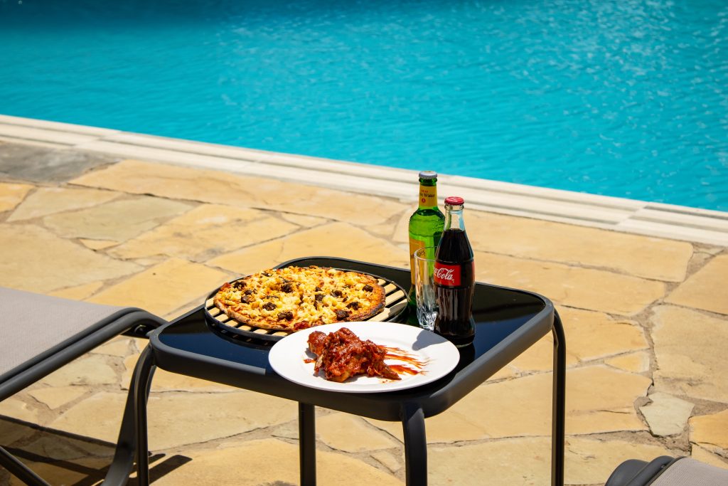 Freshly baked pizza, chicken wings, and chilled beverages served on a side table beside the swimming pool.