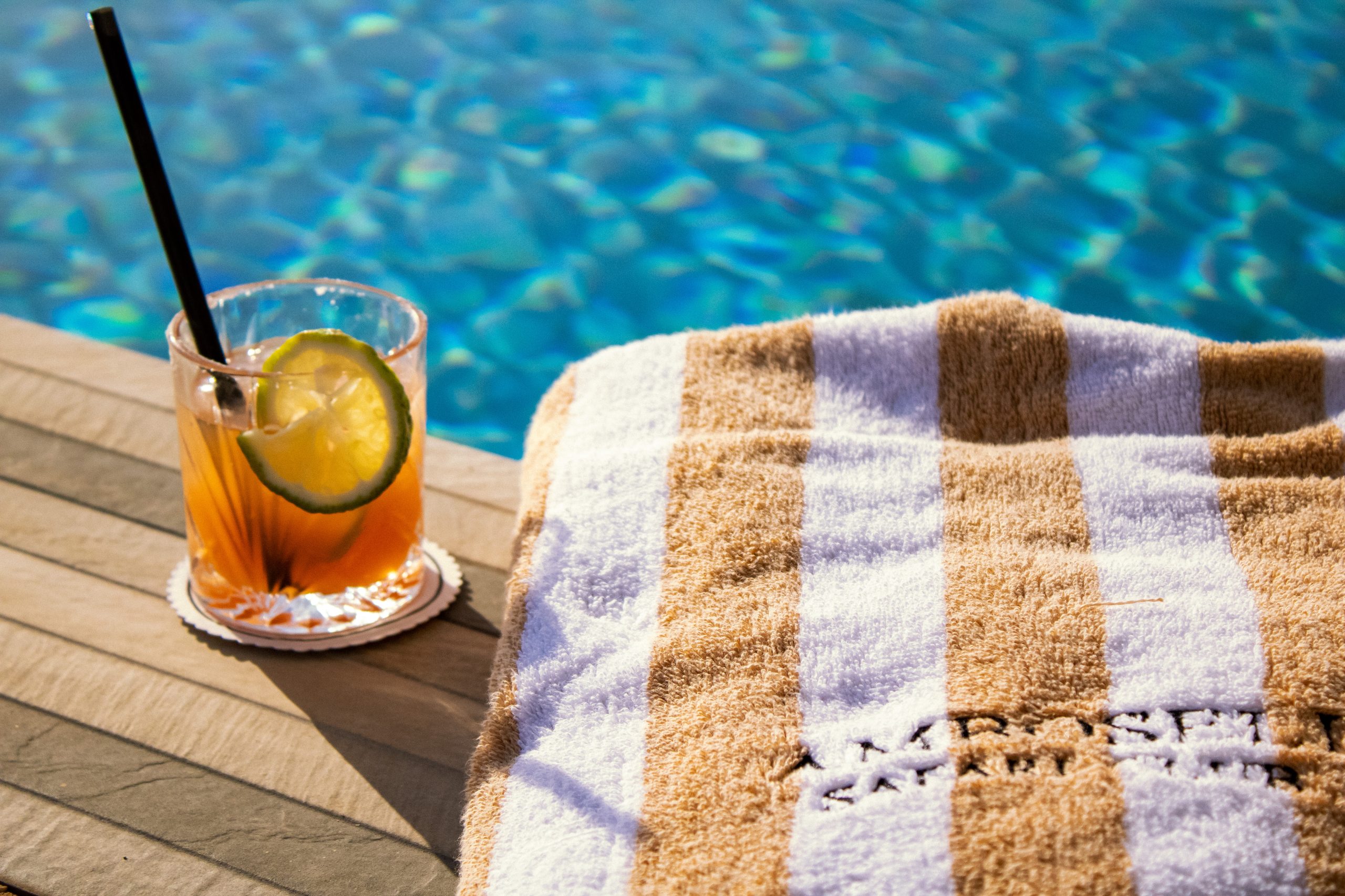 Refreshing cocktail with a lime wedge on the poolside deck beside clear blue water.